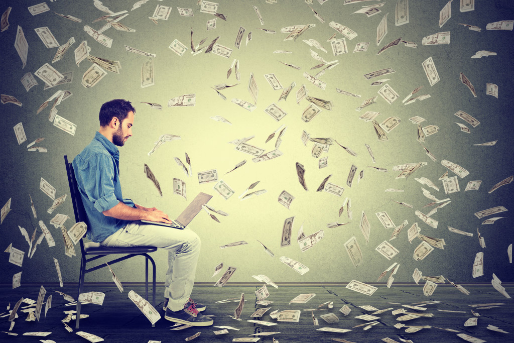 Money bills flying around a man working on his laptop