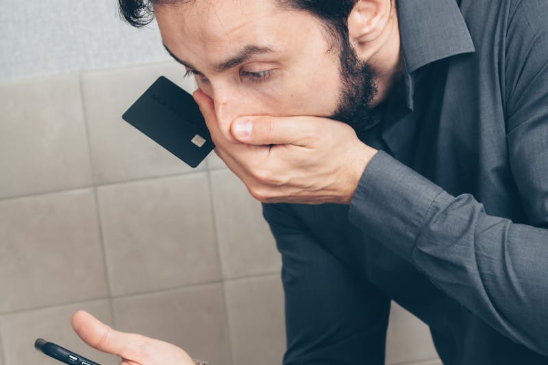 a shocked man holding his phone and credit card